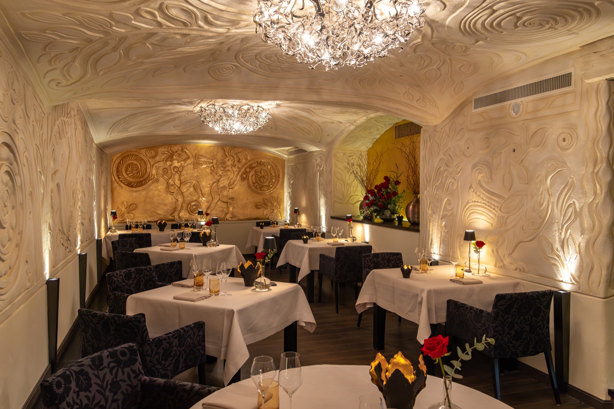 Der Gastraum des ECCO St. Moritz mit kunstvollen Reliefwänden und roten Rosen auf den Tischen